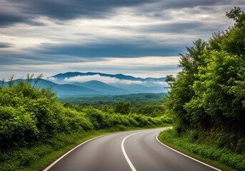 Winding road through lush green countryside towards misty mountains