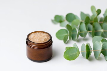 Skincare Exfoliation Ritual concept. Natural scrub jar with eucalyptus leaves on a light background.