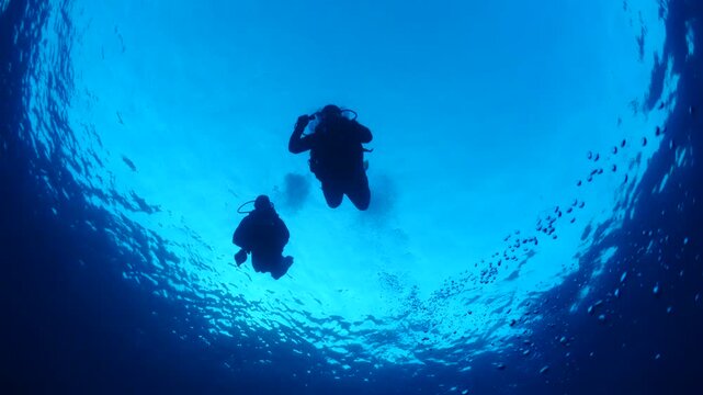 scuba divers descending underwater with bubbles around