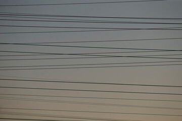 multiple overhead cables crossing pale sky, dense lines form layered grid above suburban horizon utility network pattern emphasizes repetition and infrastructure, ideal for technology