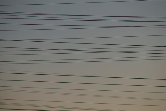 multiple overhead cables crossing pale sky, dense lines form layered grid above suburban horizon utility network pattern emphasizes repetition and infrastructure, ideal for technology