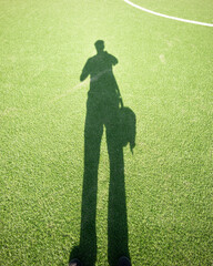 Shadow of a person with a backpack on a sunny day at a soccer field during the afternoon