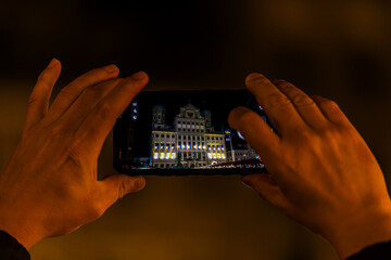 Hands holding smartphone while photographing illuminated Augsburg Town Hall at Christmas night, Germany, Augsburg, 19 December 2025