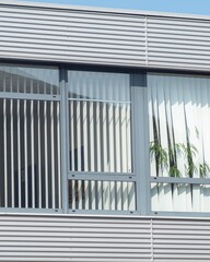 Modern building facade with vertical blinds and indoor plants visible through large windows