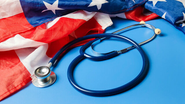 Blue Medical Stethoscope Resting Next to an American Flag Representing United States Healthcare System Reform Medical Policy and Public Health Services in America