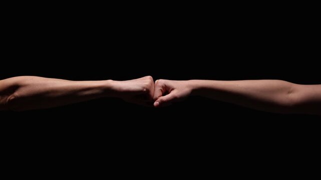 Two outstretched arms meet in a fist bump against a dark, black background, symbolizing unity and support. Significant copy space