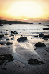Serene vertical landscape of a rocky beach at sunset with water streams reflecting golden light on the sand. Peaceful coastal scene in North Spain