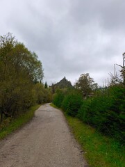 This evocative vertical shot captures a winding dirt road that serves as a powerful leading line, drawing the viewer's eye toward a distinct, pointed rocky hill in the distance. Surrounded by lush