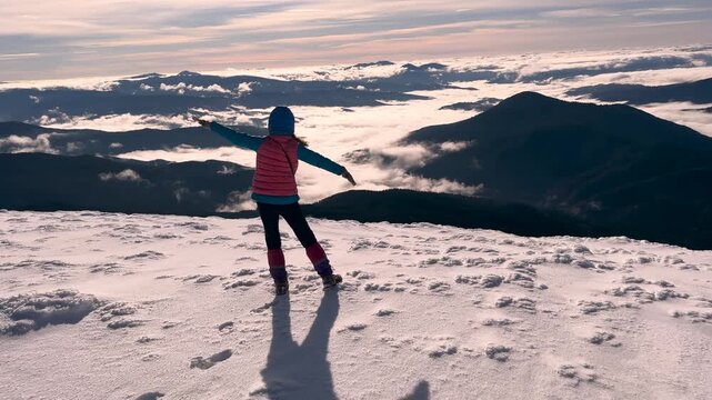 View from Hoverla in winter, Carpathians. A hiker ascends to the highest peak in Ukraine. A lone female climber with trekking poles at the summit, foggy landscape.