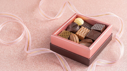 Pink and gold box of assorted chocolates with decorative ribbon on a pink background