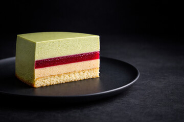 黒いプレートに置いたピスタチオとラズベリーのムースケーキ