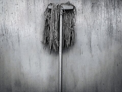 Old mop leaning against dirty concrete wall background
