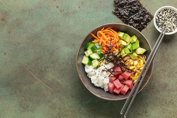 A traditional dish of Hawaiian cuisine. Poke bowl with tuna and vegetables in a bowl on the table. Top view