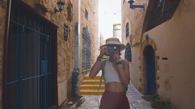 A young woman with a backpack and a camera walks along an old city street in Jaffa. A woman with a backpack walks along the street. Traveling, exploring the city.