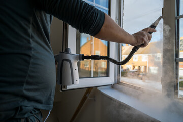Cleaning the window. A man with steam device removes dirt from the plastic window frame.