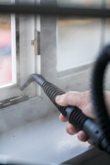 Cleaning the window. A man with steam device removes dirt from the plastic window frame.