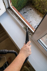 Cleaning the window. A man with steam device removes dirt from the plastic window frame.