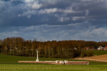 Lonely British World War One military cemetery in Flanders Fields countryside under dramatic sky, symbol of remembrance and sacrifice.