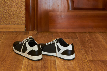 A pair of sneakers on a wooden floor indoors, Black and white sneakers near the door, New shoes on laminate