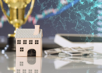 Miniature house with digital network overlay, cash, and financial chart, representing property investment, fintech, and real estate technology.