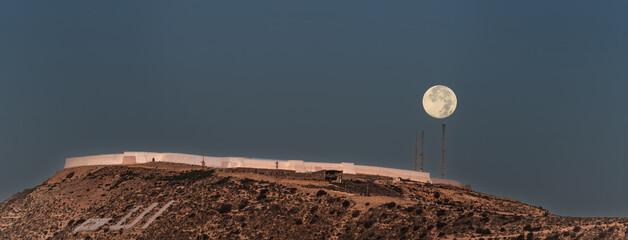 Full Moon Over Hilltop Fortification With White Barriers and Communication Towers at Dusk, Agadir, Morocco