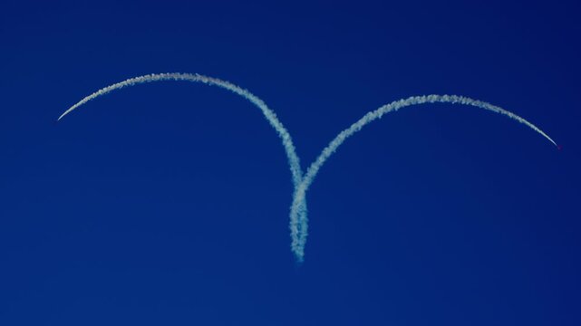 Three jet planes perform synchronized aerobatic stunt leaving heart-shaped smoke trail in clear blue sky
