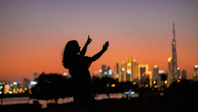 city lights Dubai skyline with gradient orange sky at sunset and silhouette of a tourist woman , background with copyspace
