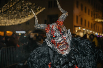 Villach, Austria - December 01, 2023: Krampuslauf festival featuring a demonic figure with horns and fangs, surrounded by festive lights and a lively crowd, showcasing traditional holiday celebrations
