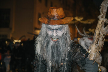 Villach, Austria - December 01, 2023: Krampuslauf festival features a menacing figure with a wooden hat and staff, showcasing traditional folklore in a vibrant street celebration with copy space