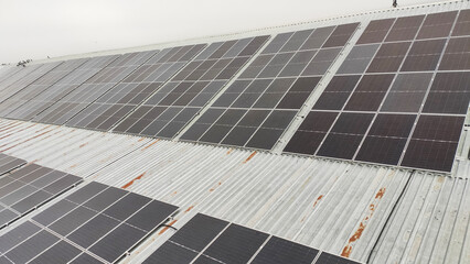 Solar panels installed on a corrugated metal roof of an industrial building under a cloudy sky