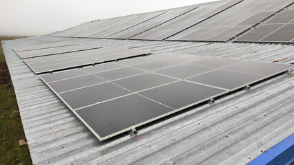 Solar panels installed on a corrugated metal roof of an industrial building under a cloudy sky