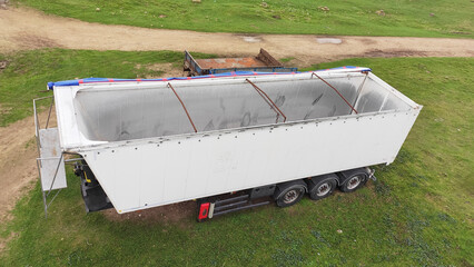 Empty white cargo semi trailer with open roof parked on green grass in rural area