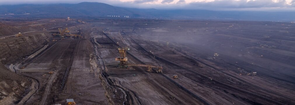 High resolution panoramic view of an open pit coal mine with mining machines, layered terrain. Industrial landscape showing large scale extraction, energy production, and environmental impact.