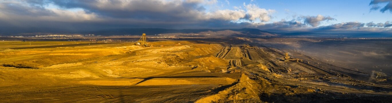 High resolution panoramic view of an open pit coal mine with mining machines, layered terrain. Industrial landscape showing large scale extraction, energy production, and environmental impact.