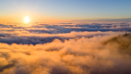 Obraz premium Golden sunrise above a sea of clouds, creating a calm and dreamy atmosphere. Warm morning light illuminates soft cloud layers, evoking freedom, serenity, and a sense of endless space.