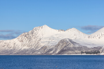 Snowy Mountain Peaks Under Clear Blue Sky and blue sea on foreground, Norway