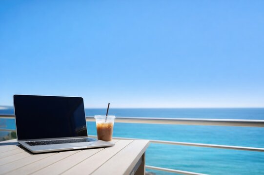 Laptop and iced coffee on balcony table with ocean view