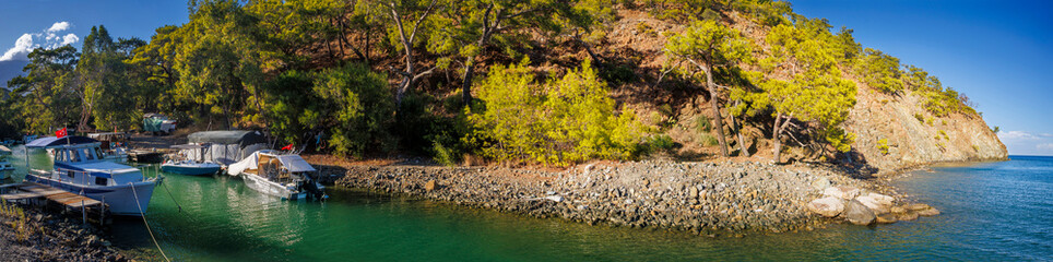 Serene Paradise Bay (Kumlubük Koyu) in Marmaris, Turkey, reveals its turquoise lagoon dotted with small boats and elegant yachts gently anchored amid dramatic cliffs and crystal-clear waters © Evgeni