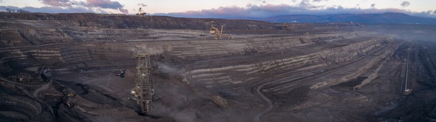 High resolution panoramic view of an open pit coal mine with mining machines, layered terrain. Industrial landscape showing large scale extraction, energy production, and environmental impact.