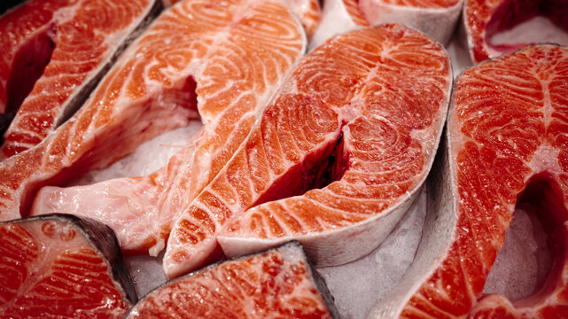 Fresh raw salmon steaks on display, bright orange fish meat with marble texture and skin, ready for cooking, seafood market background.