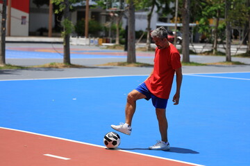 Senior Asian man in retirement age playing soccer football at outdoor court for healthy and fun...