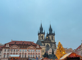 Fototapeta premium The Gothic twin towers of the Church of Our Lady before Týn rise behind a bright Christmas tree and the Jan Hus Memorial in Old Town Square, capturing a festive winter atmosphere in Prague, Czechia.