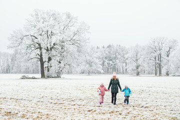 Mother walking with her children through a frozen winter landscape on a New Year&rsquo;s Eve stroll. The family is enjoying the crisp outdoors, surrounded by snow-covered fields and frost-covered trees.