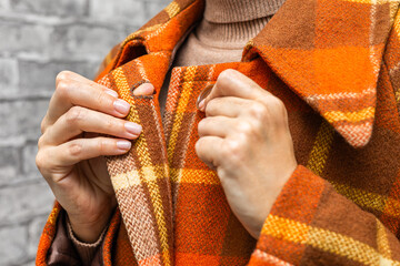 a woman fastening the top button of her coat, close-up. A woman unbuttons her coat. women's fingers fastening a button. woman putting on coat. woman trying on coat. autumn coat. top button. 