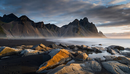 Dramatic mountain landscape features sharp jagged peaks under sky filled with stormy clouds above rocky coastline