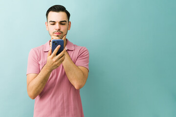 Man feeling undecided and confused while holding smartphone, choosing a new app or service online