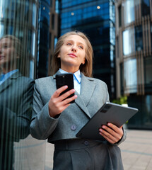 Business woman in suit using phone and tablet outdoors