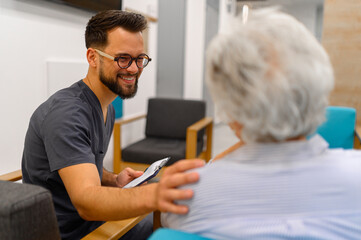Concerned male doctor with medical documents consoling senior woman while seated together in hospital during visit