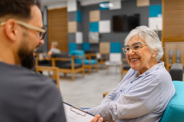 Happy senior woman listening to male ophthalmologist during routine eye assessment at hospital clinic