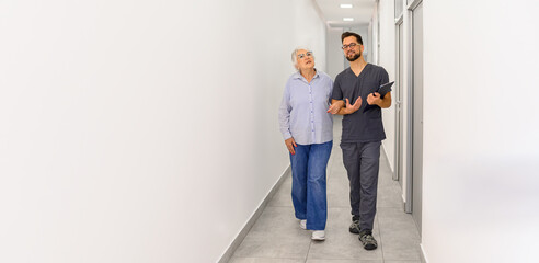 Senior woman and ophthalmologist walking arm in arm in hospital lobby discussing eye treatment and medical guidance